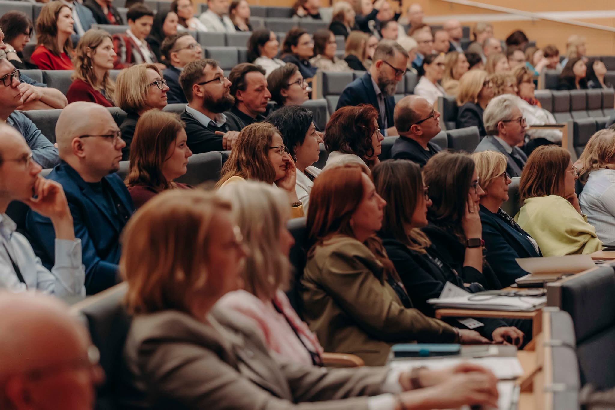 Aula wypełniona siedzącymi osobami. Widok z boku.