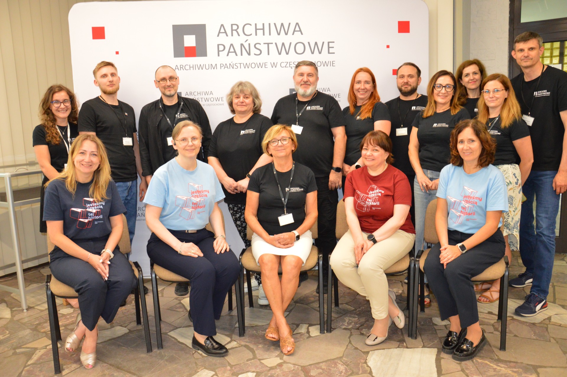 Zdjęcie grupowe. Pięć kobiet siedzi na krzesłach. Za nimi grupa stojących kobiet i mężczyzn.