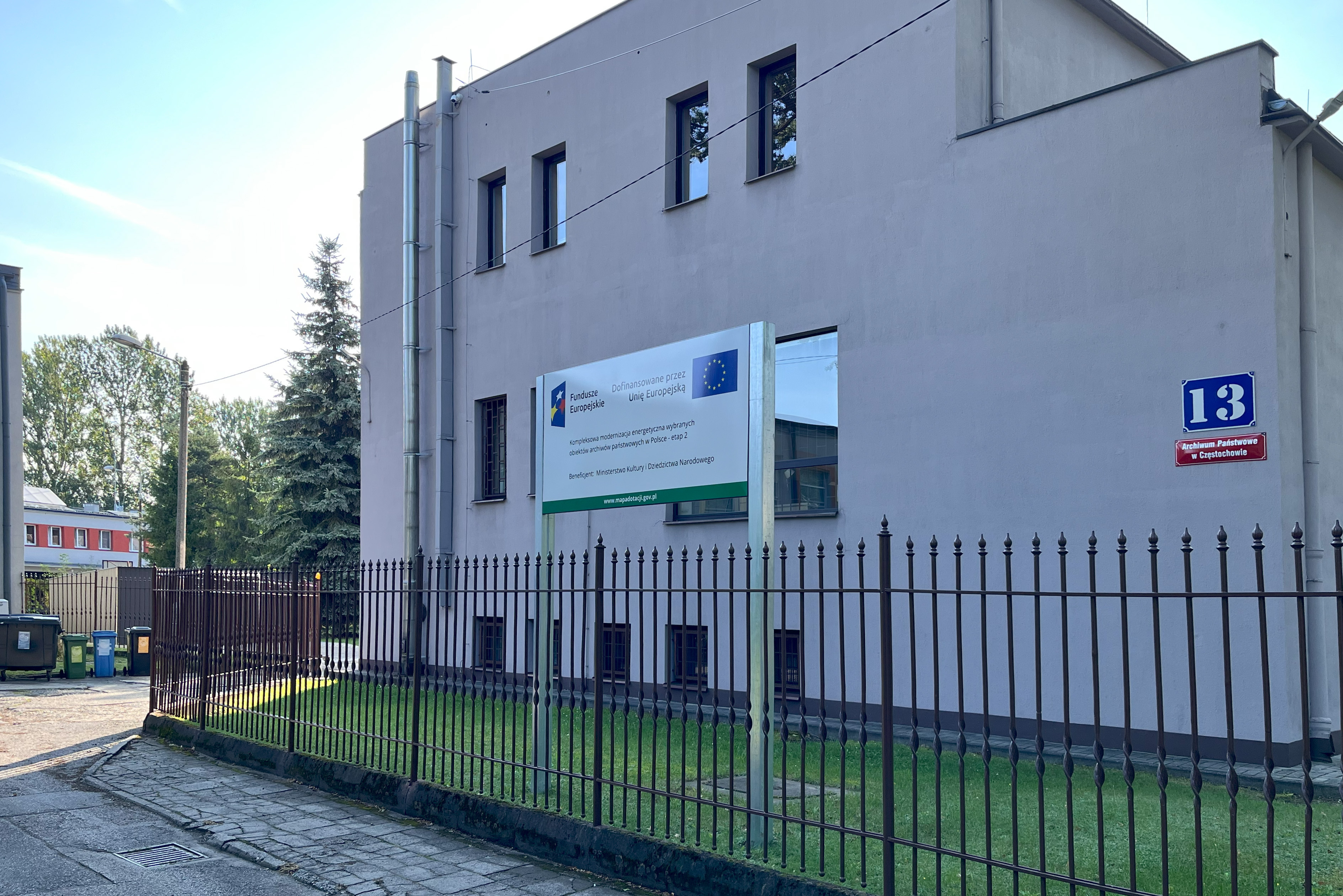 Na prawo od furtki po minięciu budynku Archiwum znajduje się brama wjazdowa na parking.